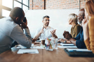 Man sitting at the head of a table presenting to a group seated at the table